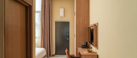 Een hotelkamer met een bed, een bureau met stoel, een televisie en een deur.
