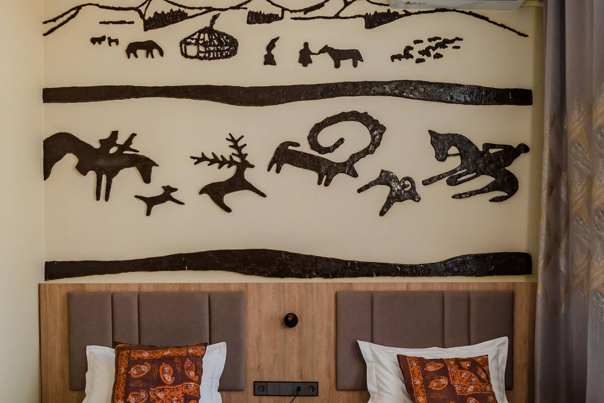 Habitación de hotel con dos camas, cabecero de madera, mural en la pared y alfombra estampada.