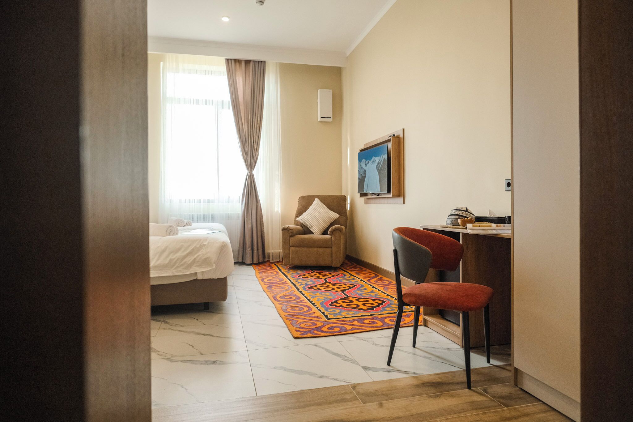 A hotel room with a bed, a chair, a desk, and a TV.