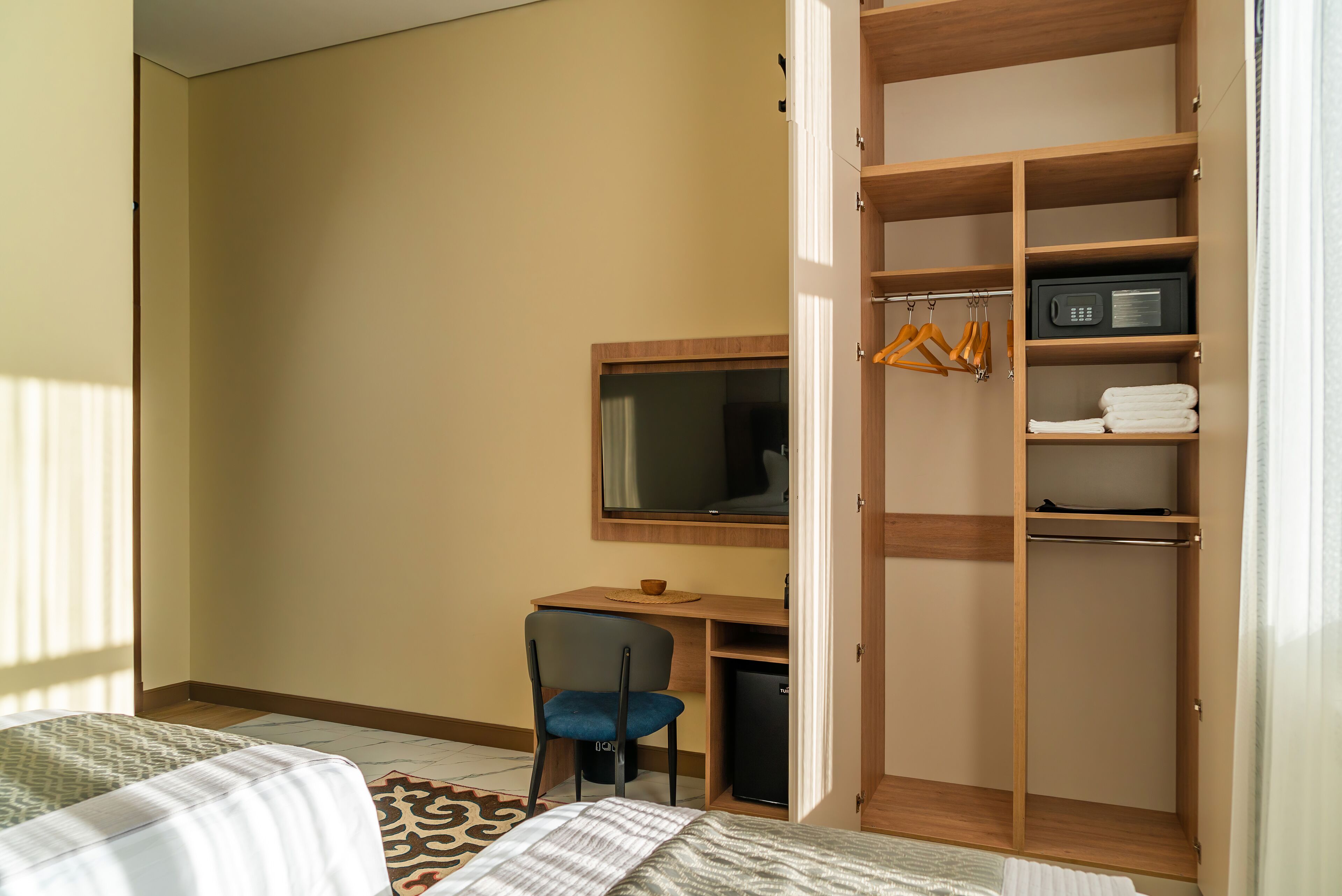 A hotel room with a bed, a desk with a chair, a TV, and a wardrobe.