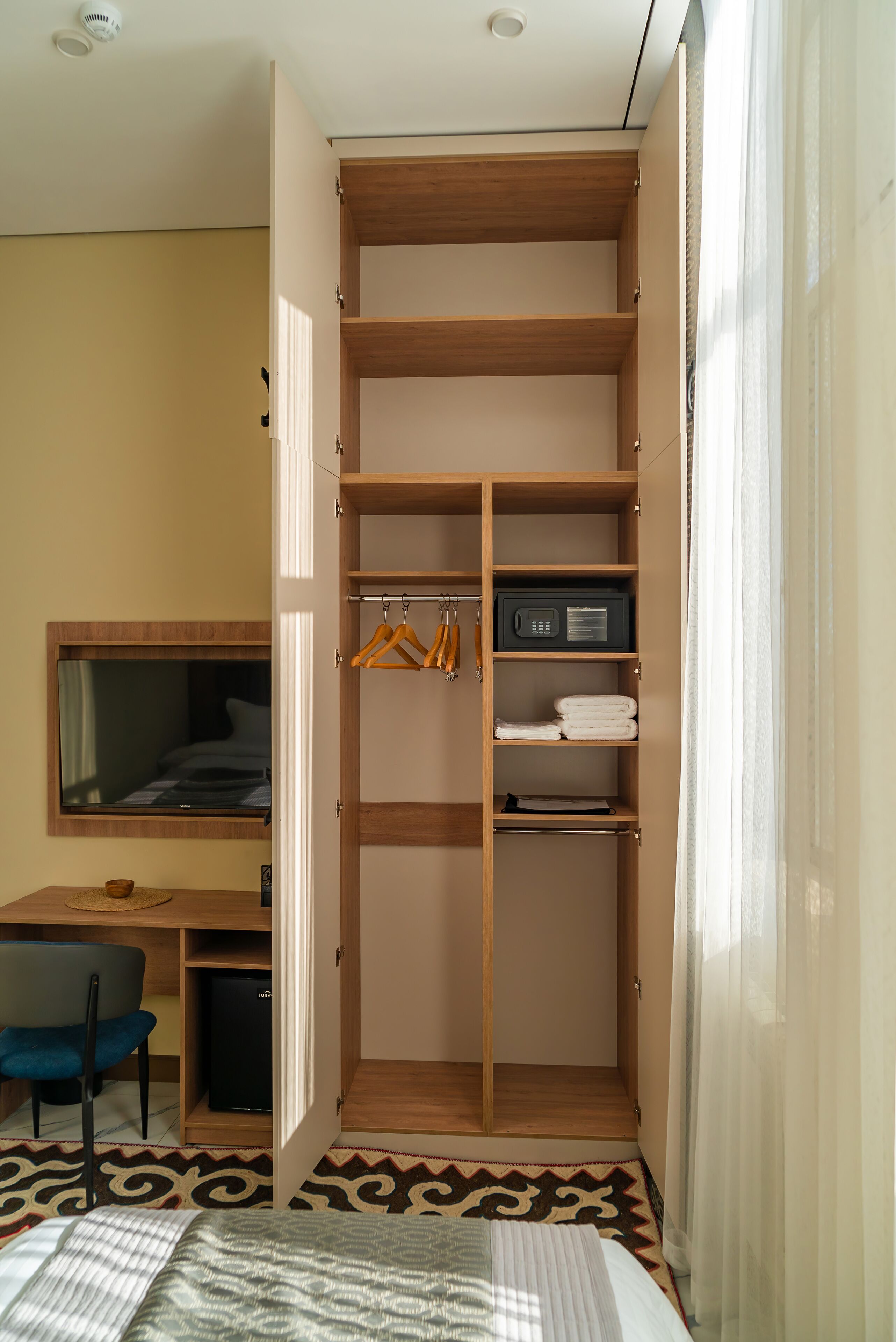 A bedroom with a bed, a desk, a chair, a wardrobe, and a window.