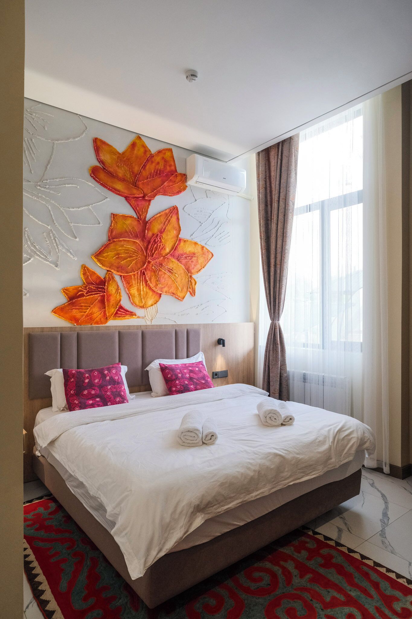 Una habitación de hotel con una cama grande, un cabecero con diseño floral y una ventana con cortinas.