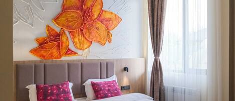 Una habitación de hotel con una cama grande, un cabecero con diseño floral y una ventana con cortinas.