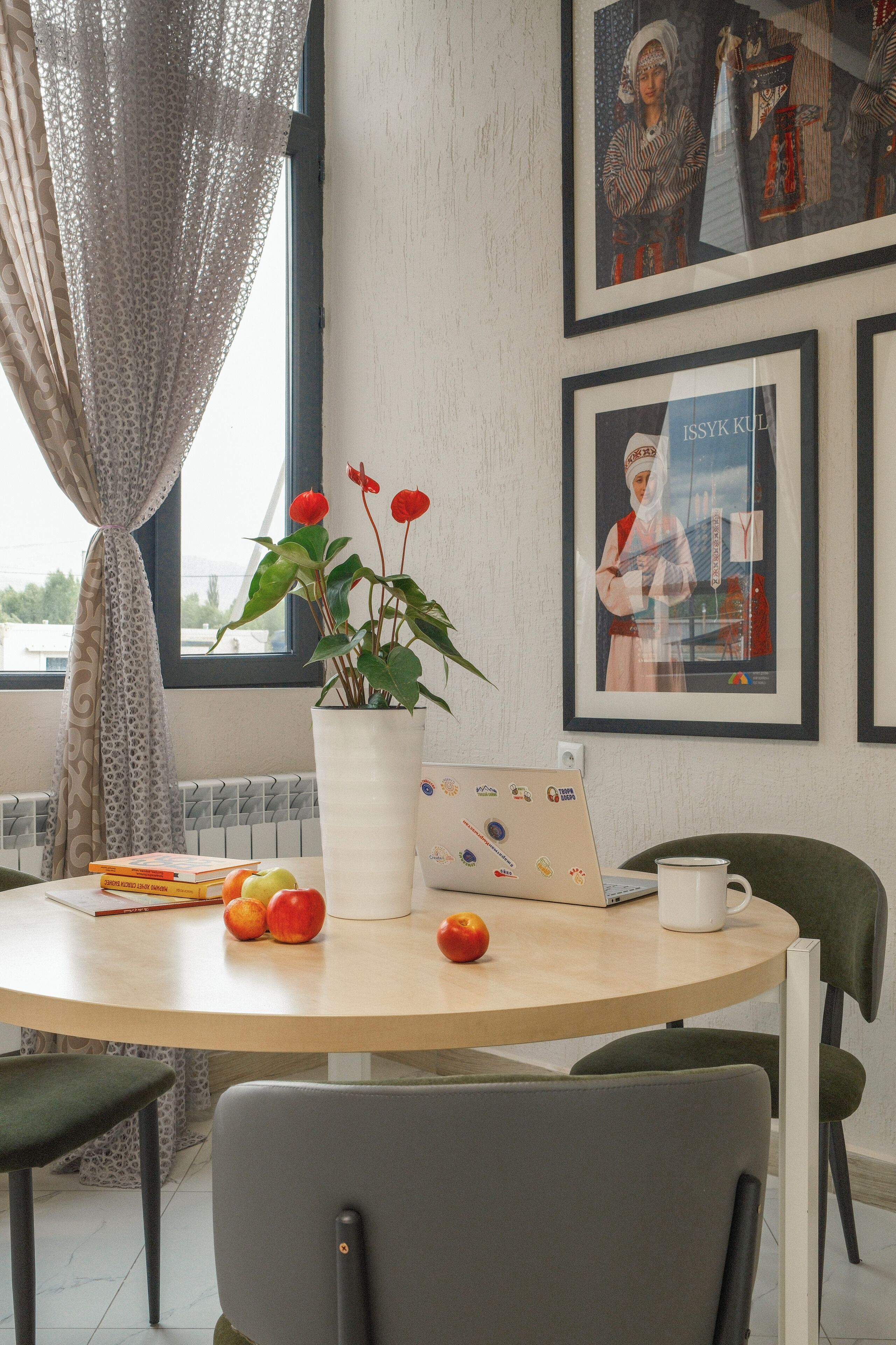 A round table with a laptop, a mug, and a potted plant with red flowers.