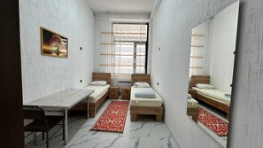 A narrow room with two beds, a desk, and a chair.