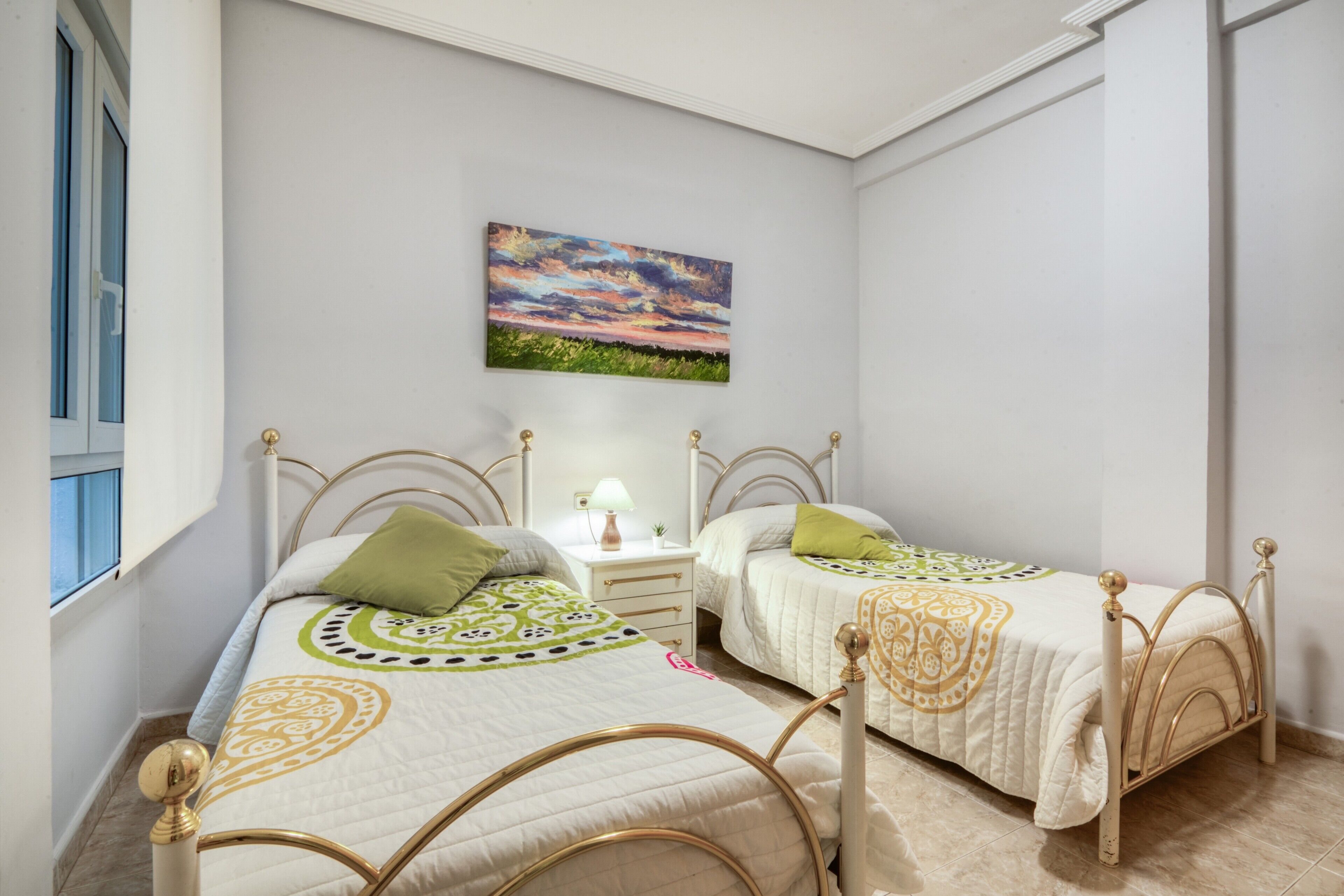 Una camera da letto con due letti, un comodino, una lampada e un quadro appeso al muro.