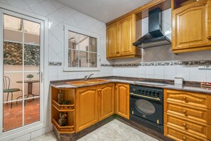 Une cuisine avec des meubles de rangement en bois, un poêle noir et une fenêtre donnant sur un patio.