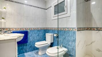 Un bany amb vàter, bidet i rentapel, rajoles blaves i blanques, i una finestra.