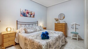 Un dormitorio con cama, mesita de noche, cómoda, espejo y una obra de arte en la pared.