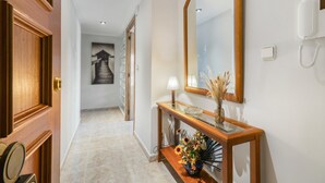 Un pasillo con una puerta de madera, una consola con un florero, un espejo y un teléfono en la pared.