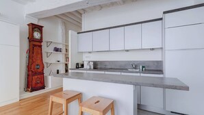 Une cuisine moderne avec des meubles blancs, un tabouret de bar en bois et une grande horloge en bois.