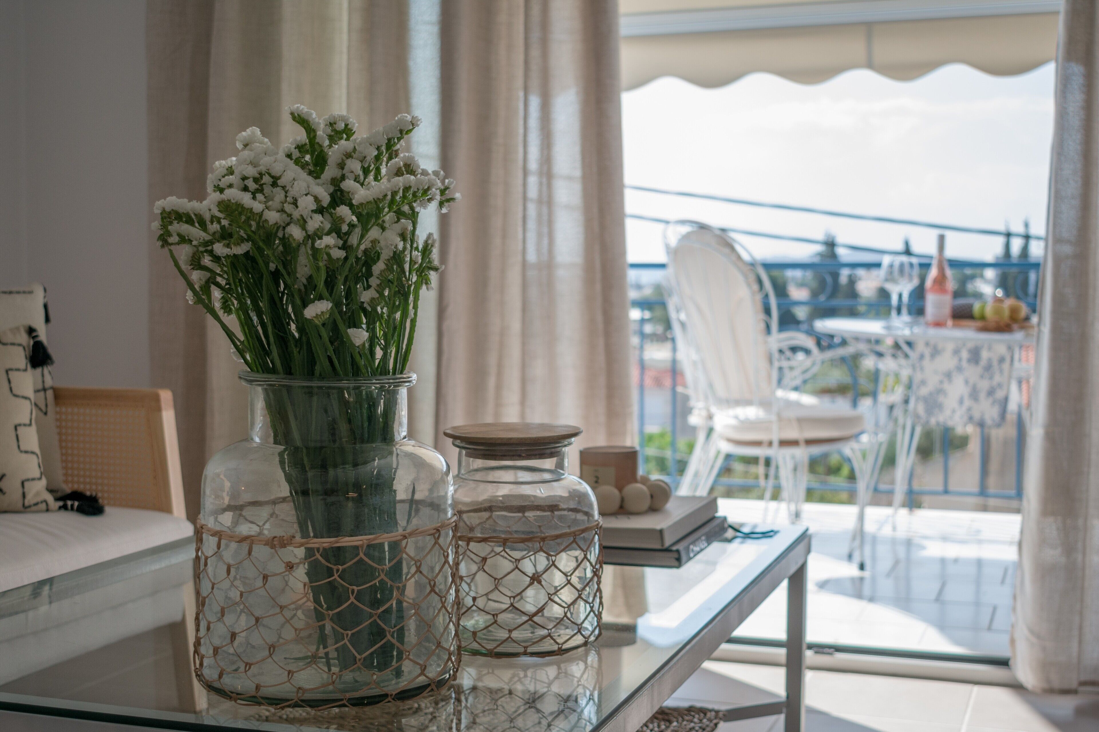 Une table en verre ornée d’un vase de fleurs blanches, d’un bocal en verre et d’un panier en osier.