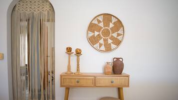 A room with a macramé wall hanging, a woven wall art piece, a wooden console table with drawers, and a small stool.