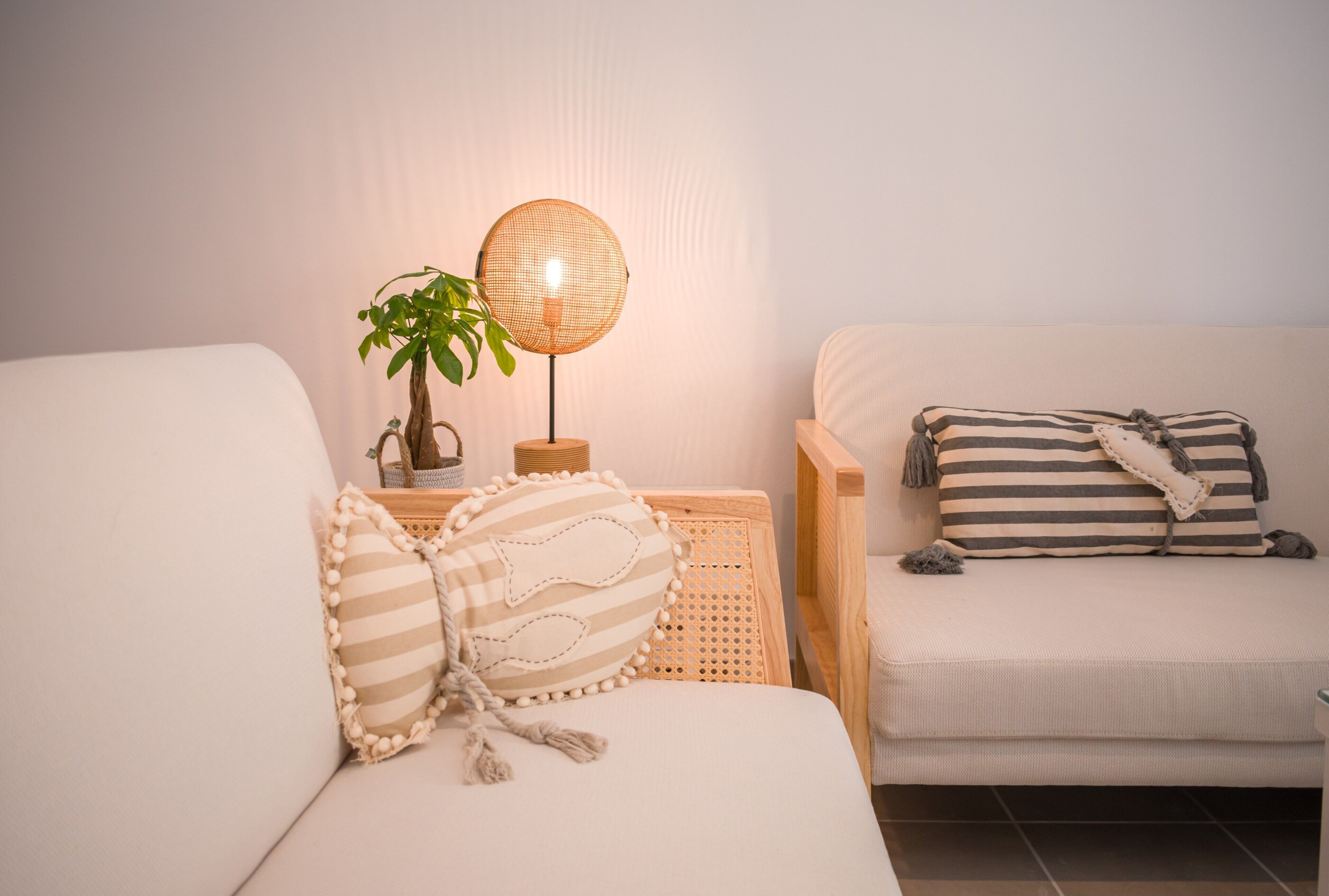 A cozy room with a sofa and a chair, each with decorative pillows. A floor lamp and a potted plant are on a wooden side table.
