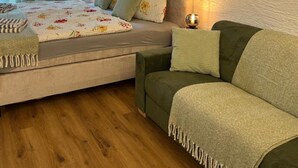 A bedroom with a bed, a green sofa, a bedside table with a lamp, and a window with curtains. - Studio "Andys Edelweiss" in Leutasch (Leutasch)