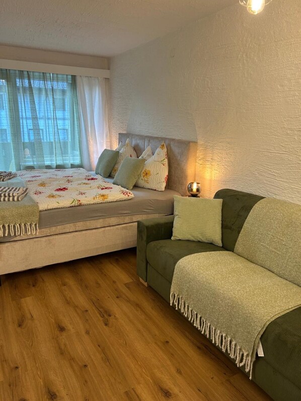 Une chambre à coucher avec un lit, un canapé vert, une table de chevet avec une lampe et une fenêtre avec des rideaux.