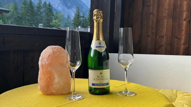 A table with a bottle of wine, two glasses, and a salt shaker on a yellow tablecloth, with a mountain view in the background. - Studio "Andys Edelweiss" in Leutasch (Leutasch)