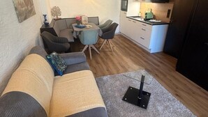 Un espacio habitable compacto con sofá, una pequeña mesa de comedor, zona de cocina e iluminación en el techo.