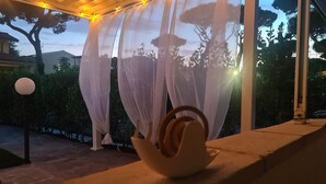 Une urne blanche et décorée, posée sur une corniche en pierre, avec une guirlande lumineuse au-dessus et un rideau blanc et transparent en arrière-plan.