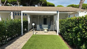 Une villa blanche avec un toit en tuiles, un patio couvert avec deux chaises et une table, et une pelouse bien entretenue.