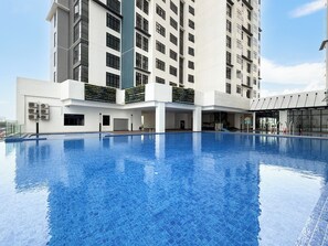 A modern hotel with a large indoor swimming pool, a covered outdoor area, and a high-rise building in the background.