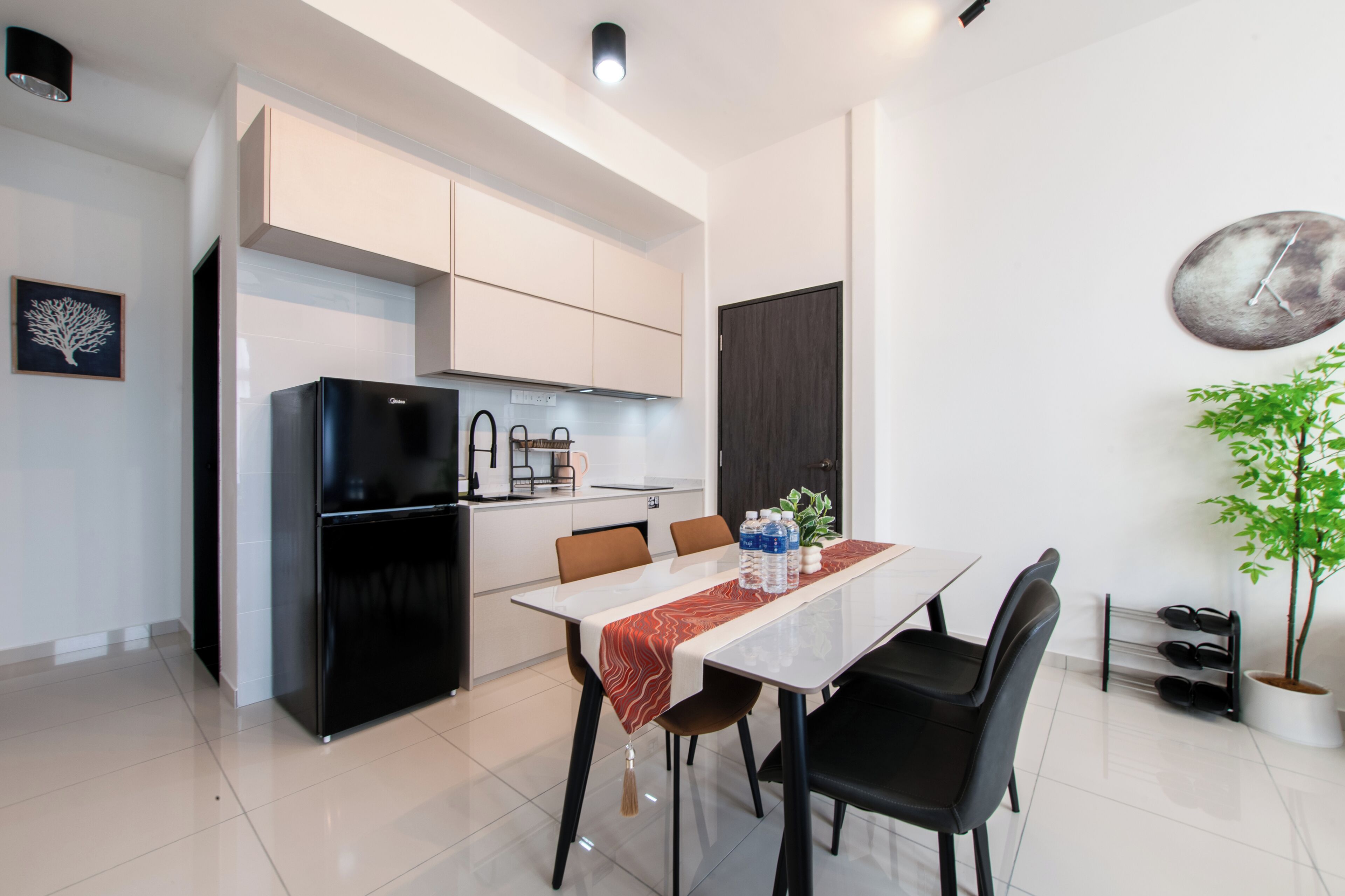 Una cocina moderna con armarios blancos, un refrigerador negro y un comedor con mesa y sillas.