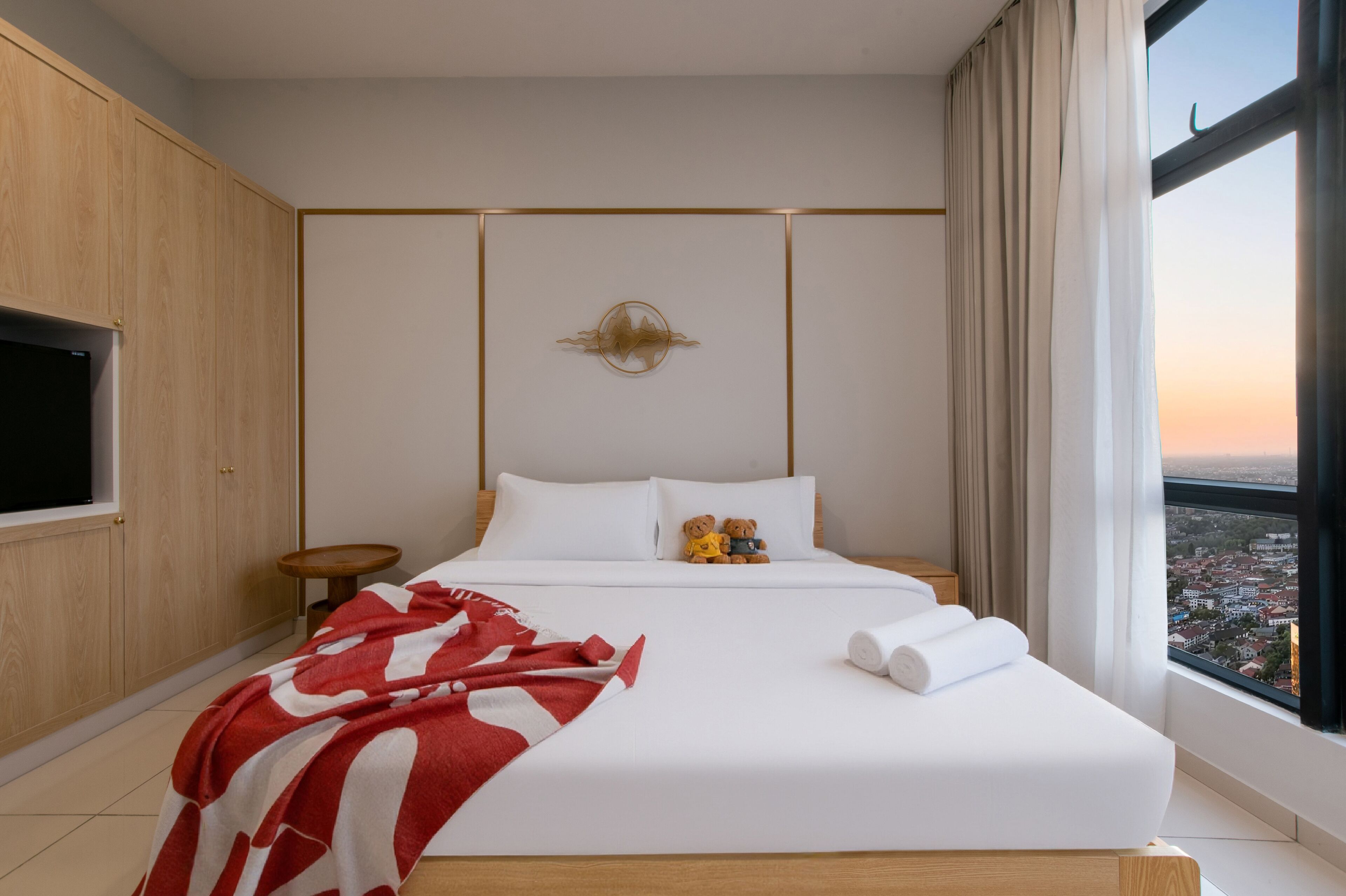 A modern hotel room with a large bed, a TV mounted on the wall, and a view of the city through the window.