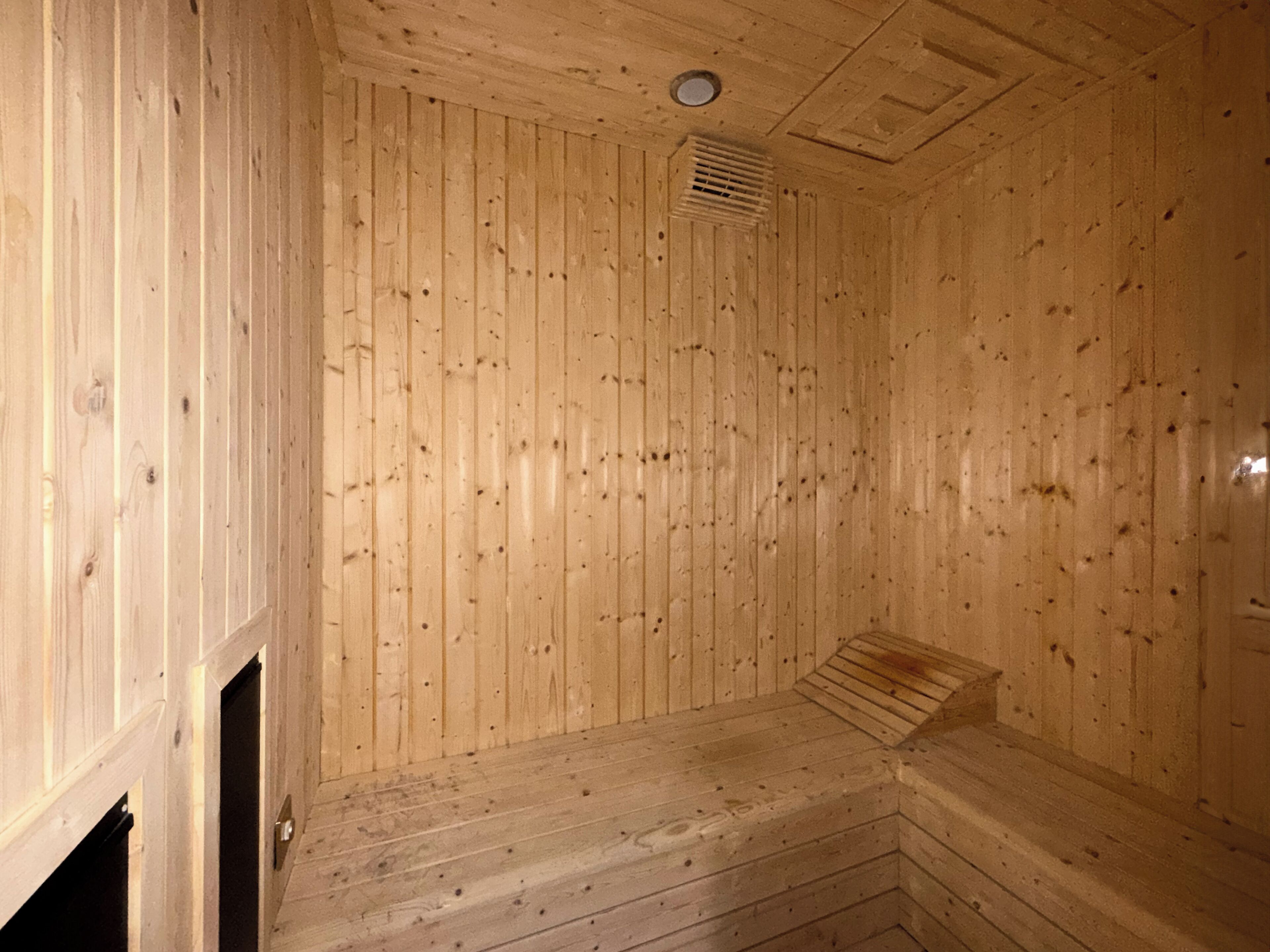 Un sauna de madera con un banco, una rejilla de ventilación y una puerta.