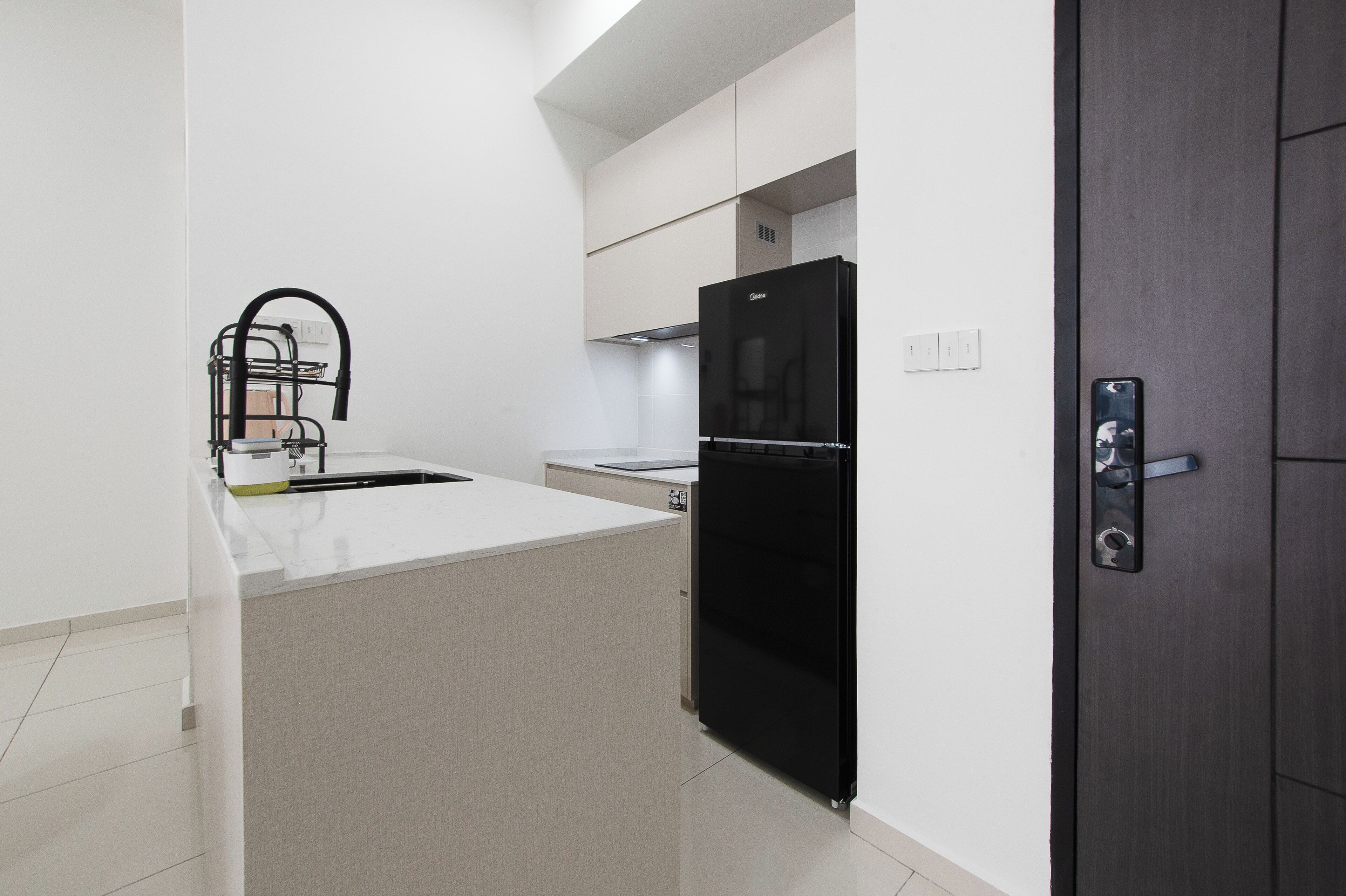 A modern kitchen with a black refrigerator, white countertops, and a dark wooden door.