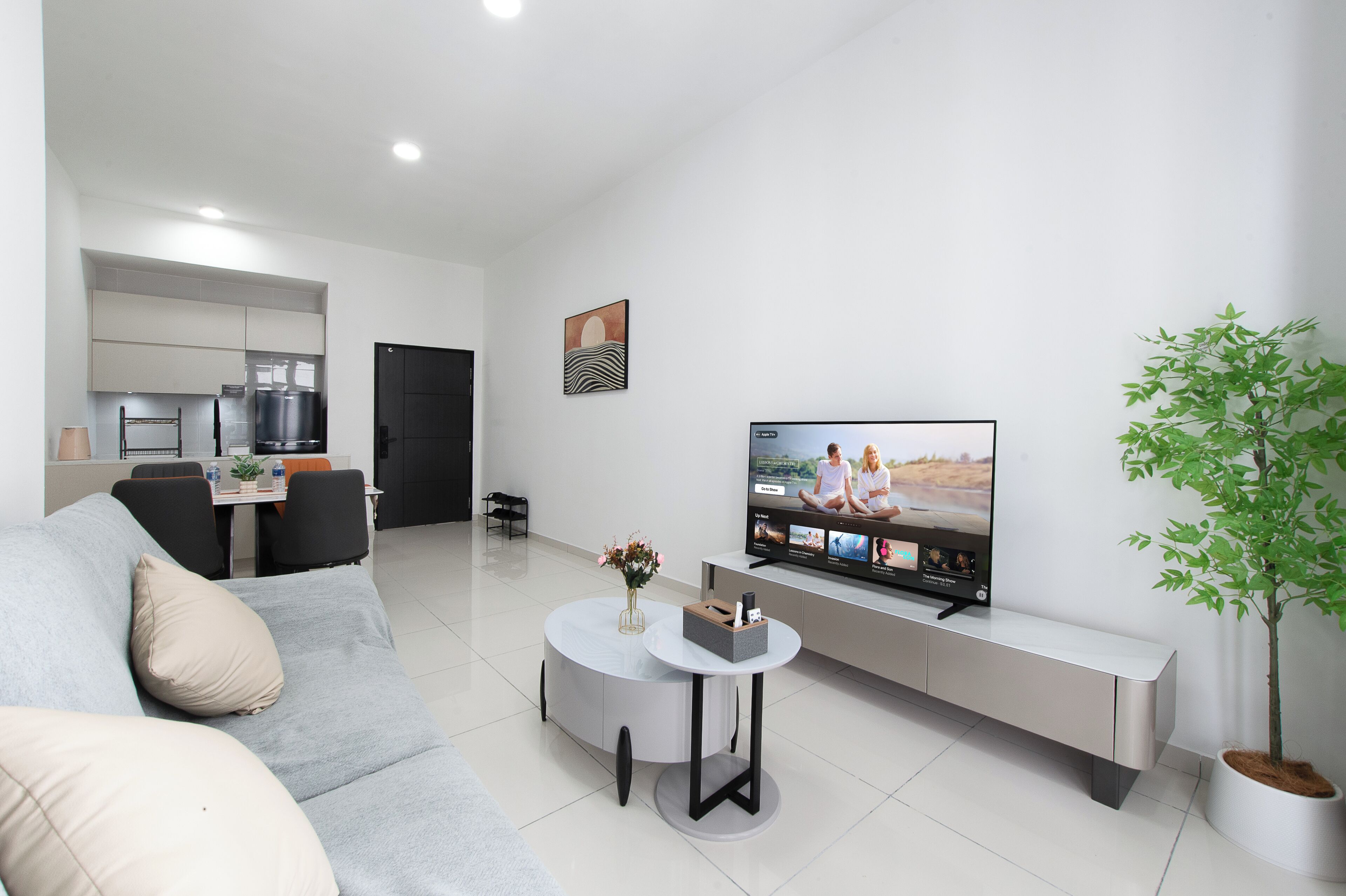 Una sala moderna con un sofá gris, una mesa de centro, un televisor de pantalla plana, un comedor con sillas y una planta en maceta.