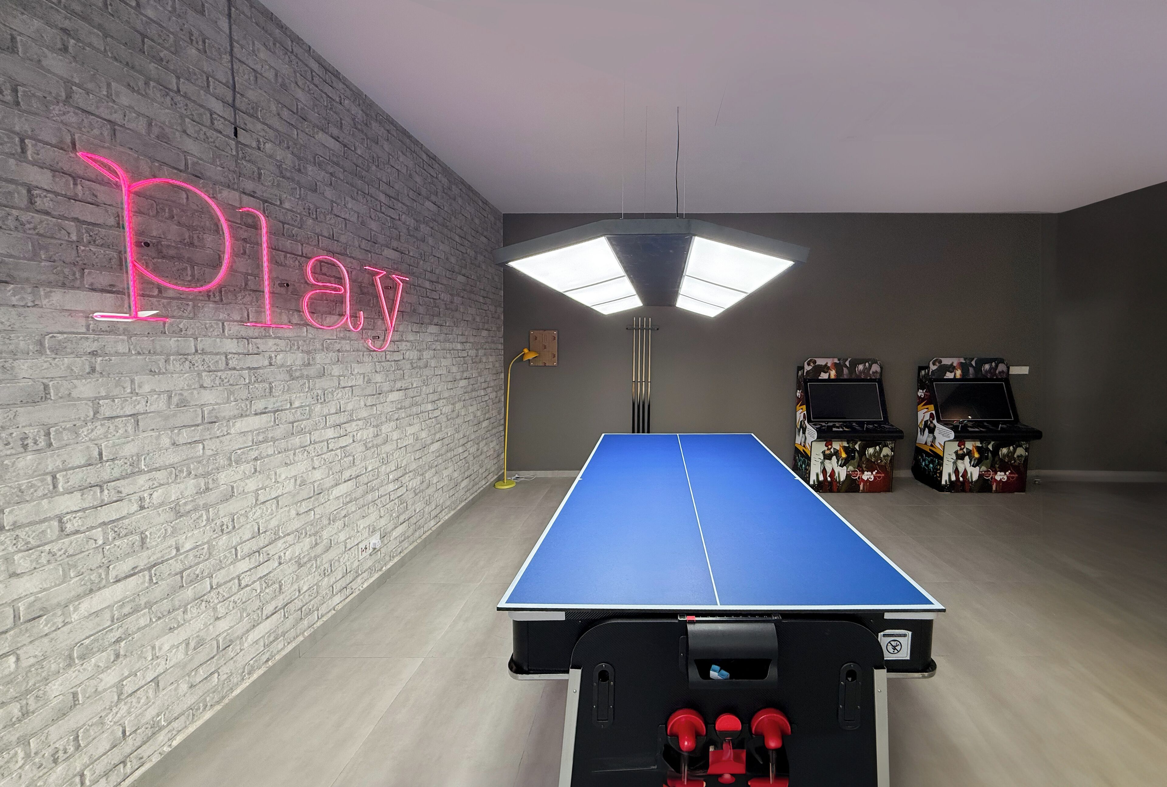 A ping pong table in a room with a brick wall and a neon sign that reads "Play".