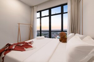 A hotel room with a large window, a bed, a teddy bear, and a wooden hanger.