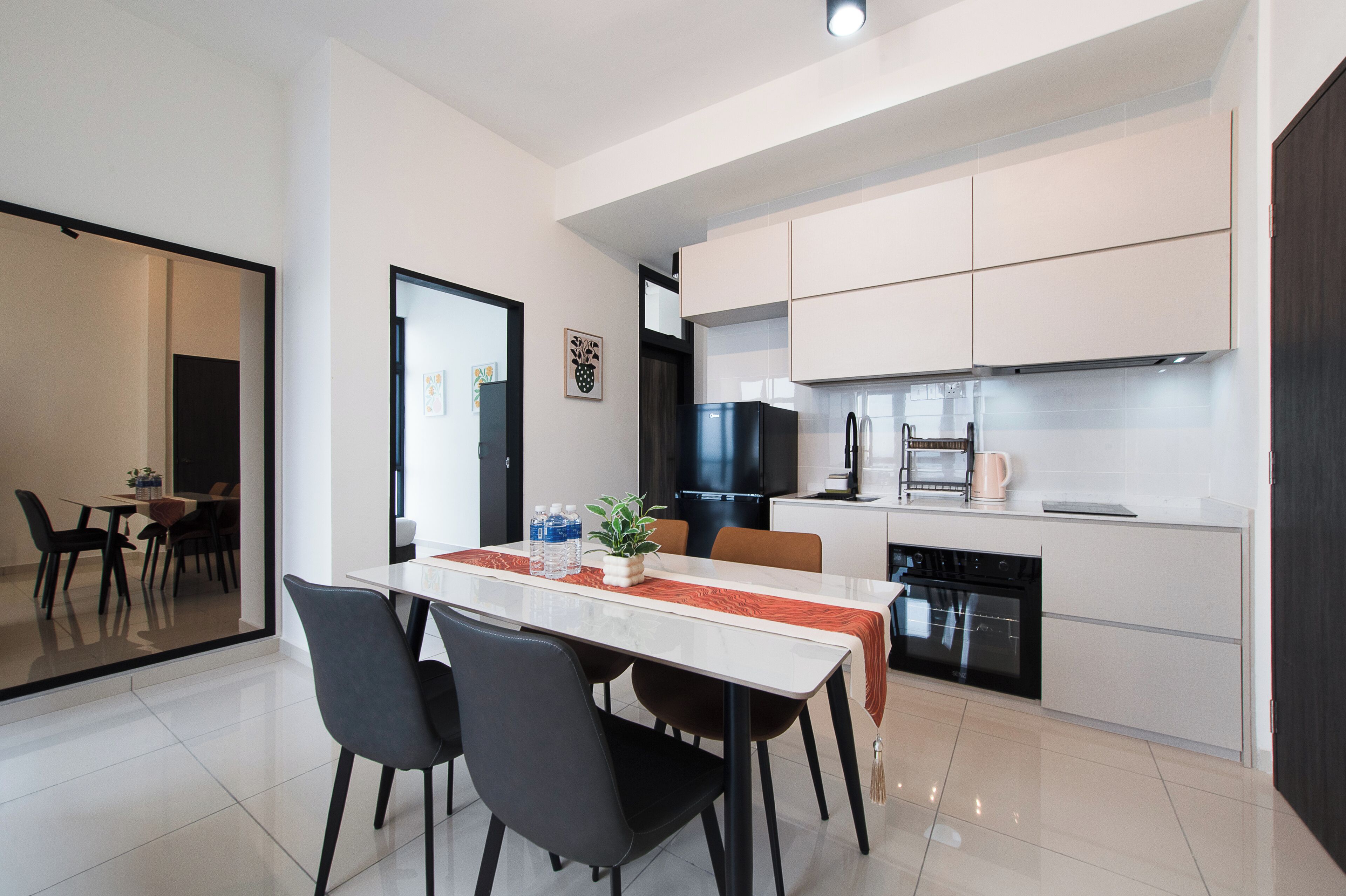 Una cocina moderna con armarios blancos, un refrigerador negro y un comedor con mesa blanca y sillas negras.