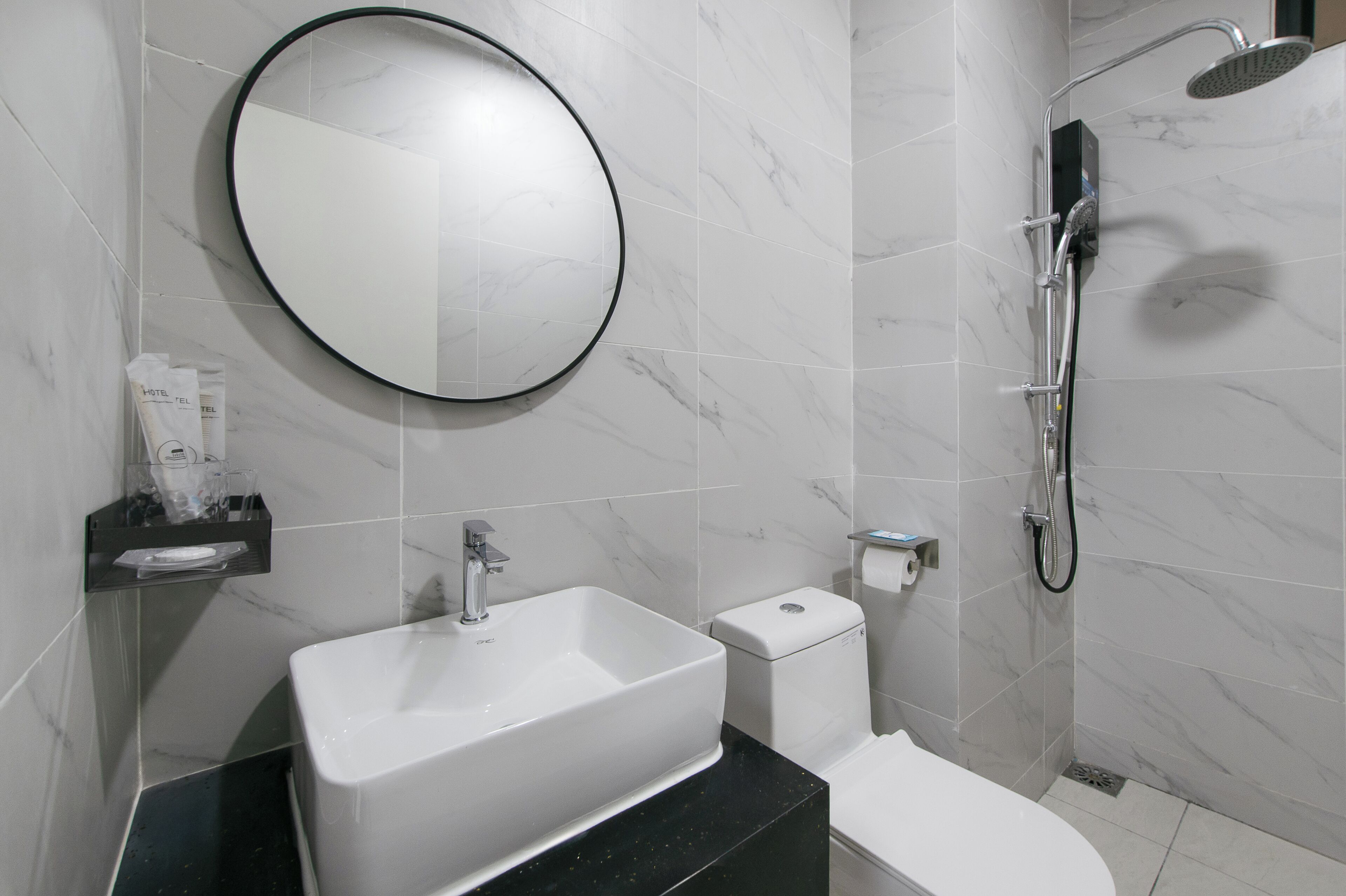 A modern bathroom with a white sink, a round mirror, a handheld showerhead, and a toilet.