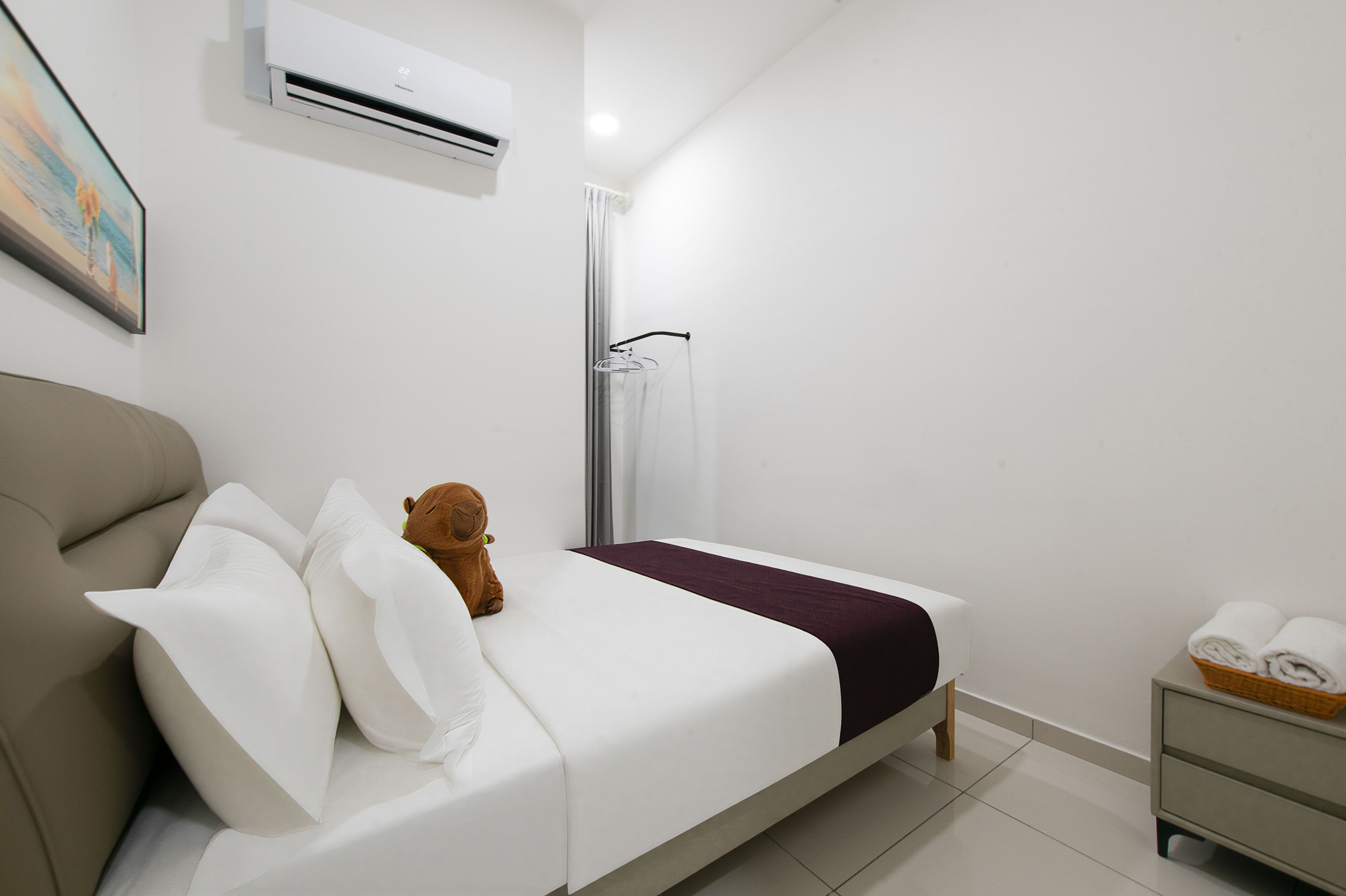 A bedroom with a bed, a teddy bear, a shower, and a nightstand with towels.