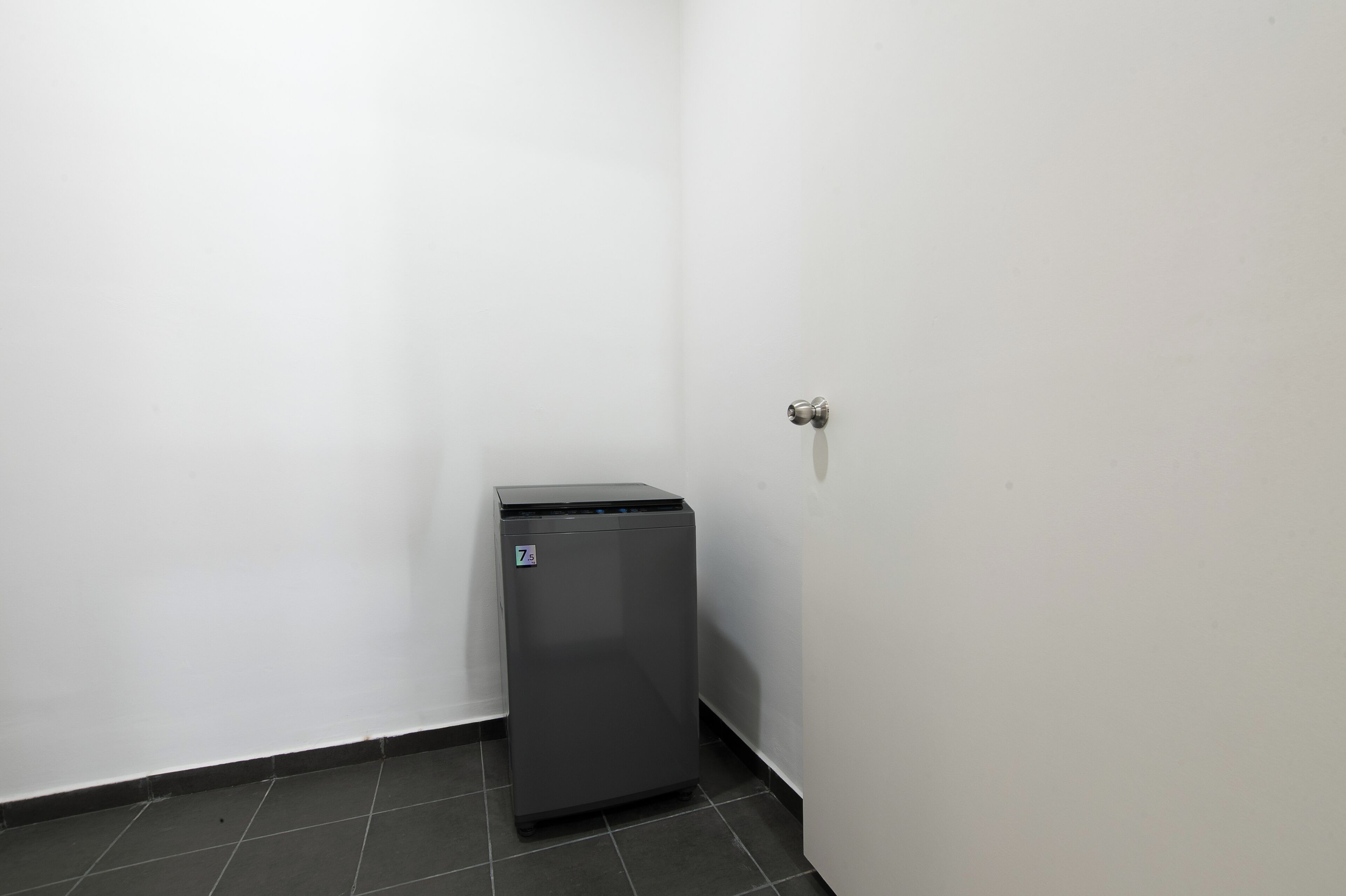 A compact, dark-colored refrigerator in a corner of a room with white walls and dark tiled flooring.