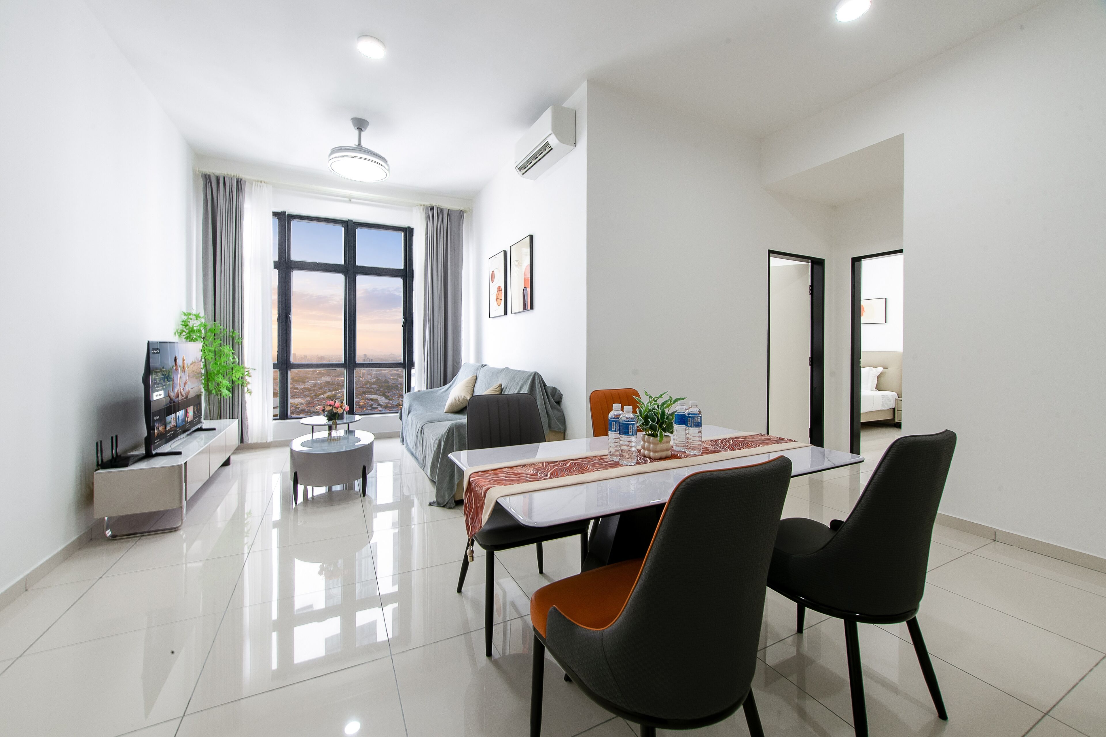 A modern living room with a dining area, large windows, and a flat-screen TV.