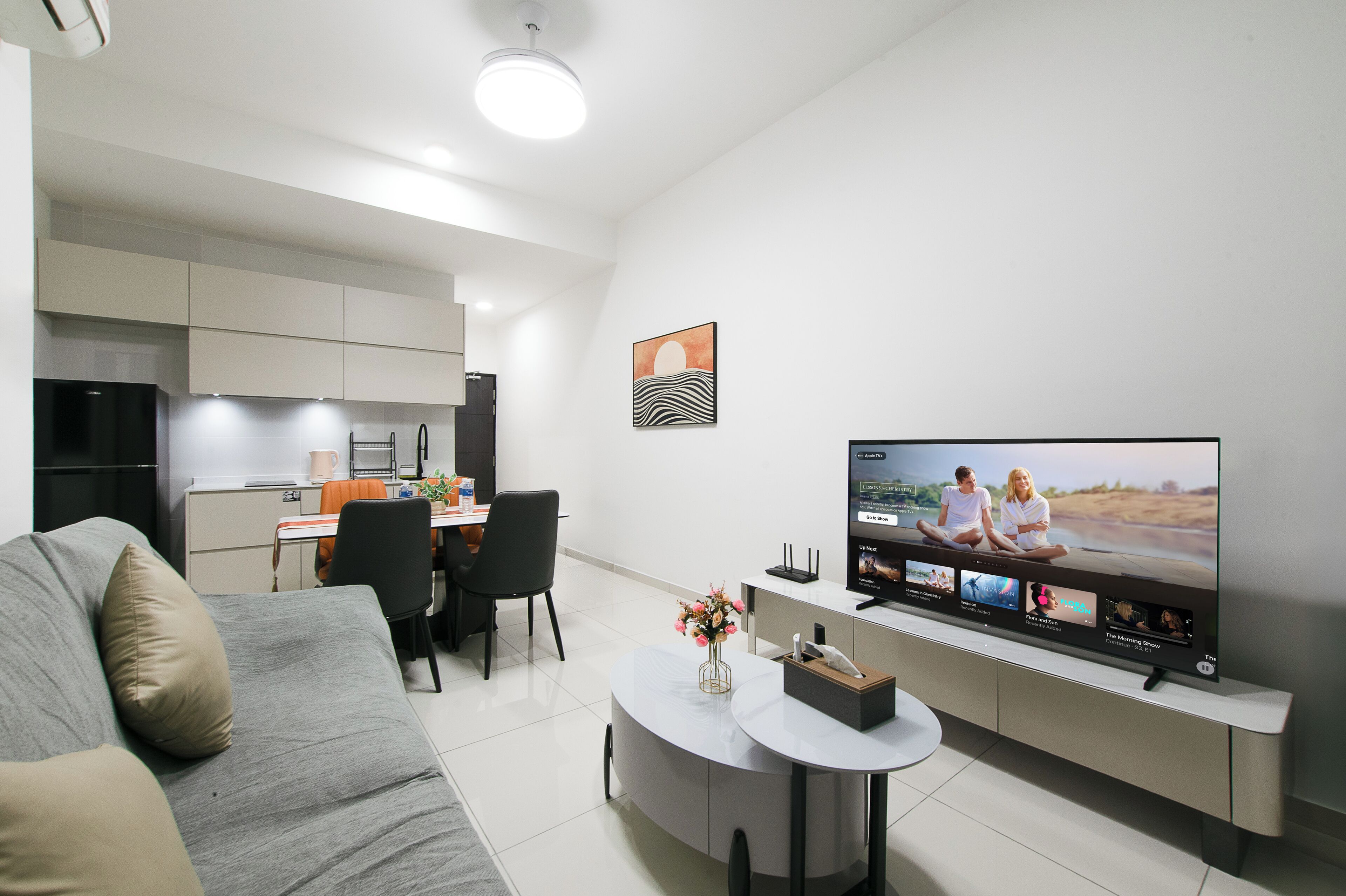 A modern living room with a flat-screen TV, a sofa, a dining area, and a kitchen.