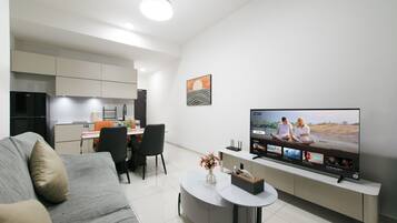 A modern living room with a flat-screen TV, a sofa, a dining area, and a kitchen.