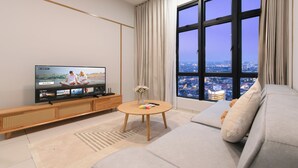 A modern living room with a large TV, a wooden coffee table, a sofa, and a view of a cityscape through large windows. - Space Residency by A----Walk 100m to KSL (Johor Bahru)