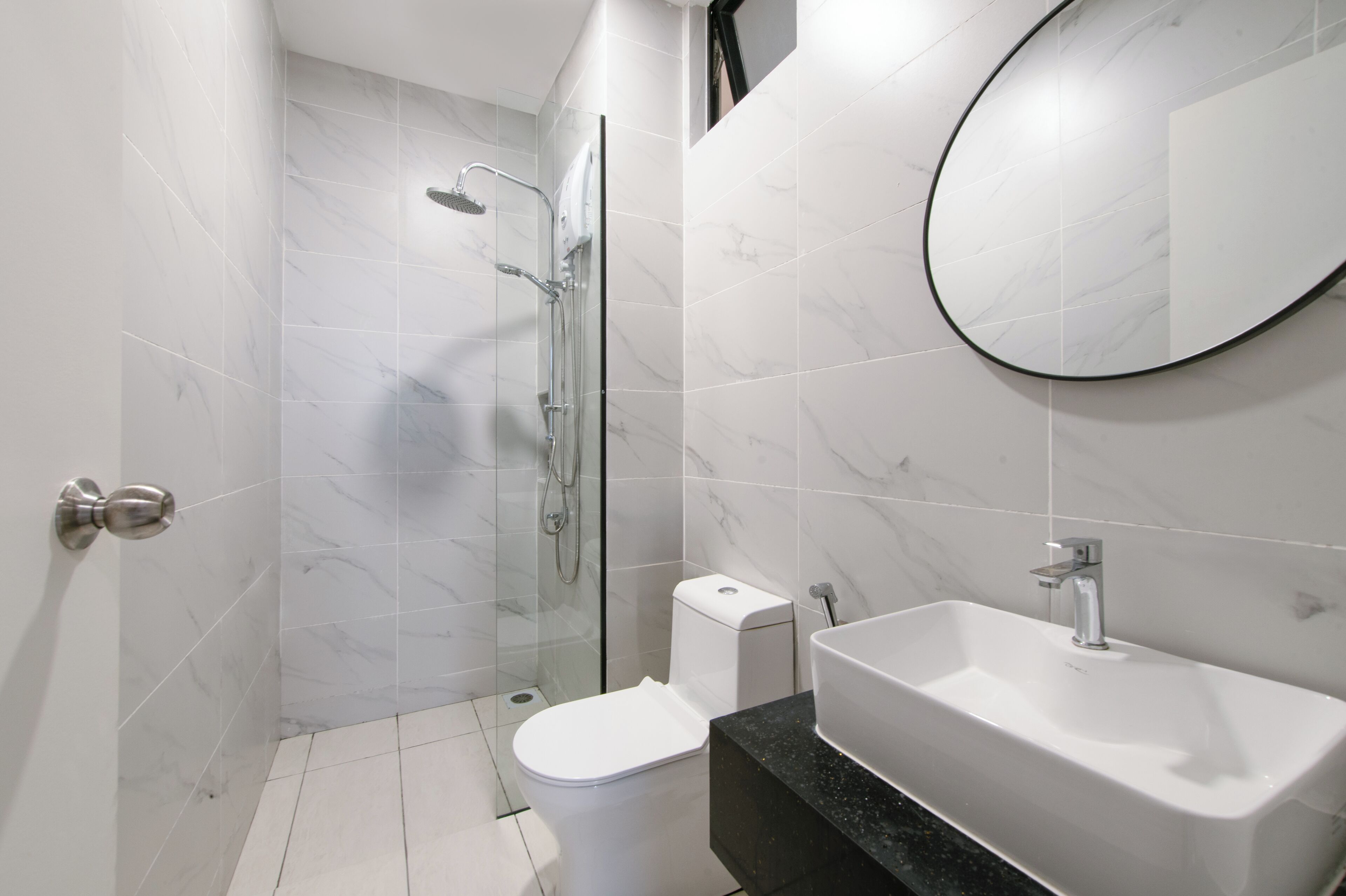 A modern bathroom with a glass-enclosed shower, a white toilet, and a large sink with a mirror above it.