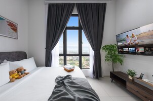 A hotel room with a large bed, a TV mounted on the wall, a window with curtains, and a view of the cityscape.