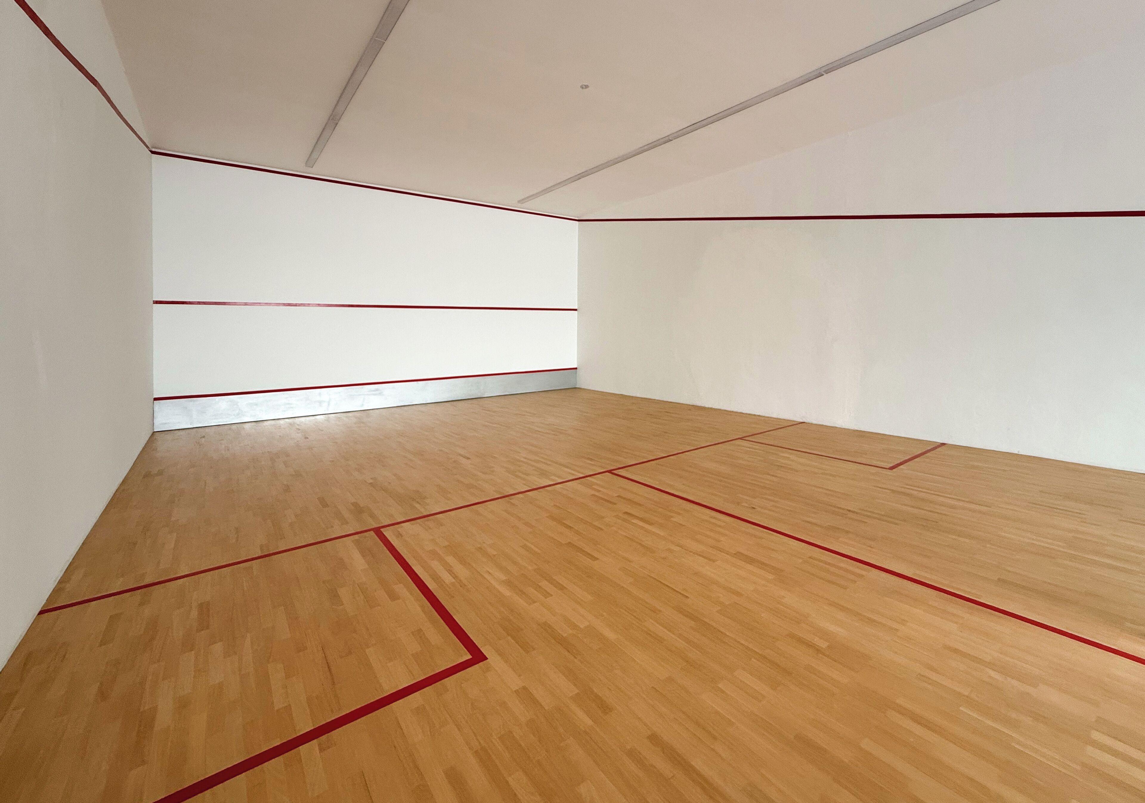 A squash court with wooden flooring and red boundary lines.