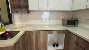 A kitchen with white cabinets, a microwave, and a small shelf with plants.