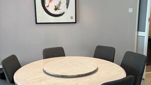 A round table with six chairs, a framed abstract painting on the wall, and a door to the right.