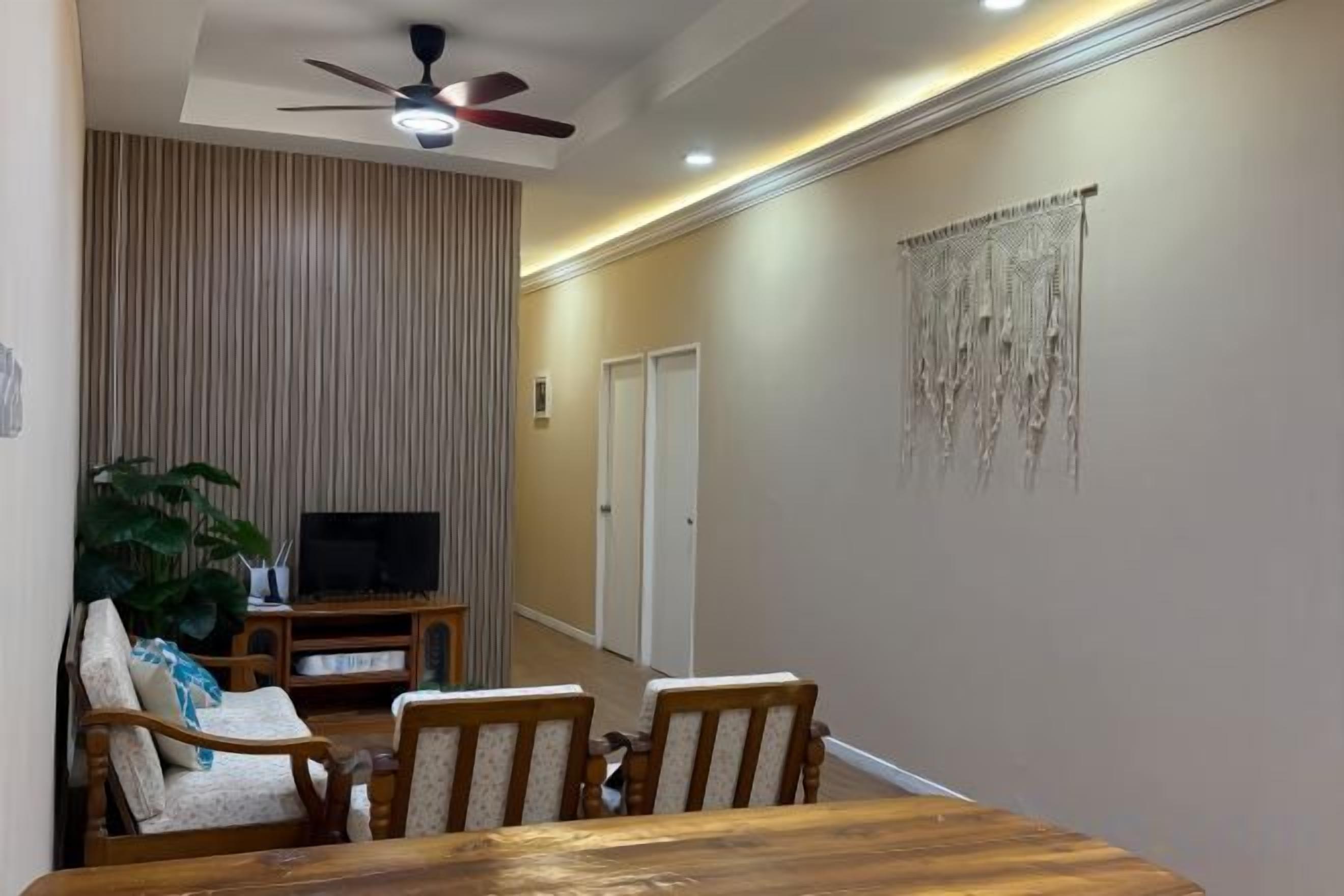 A dining area with a wooden table and chairs, a television on a stand, and a plant.