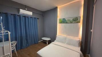 A bedroom with a bed, a small table, a chair, a wall-mounted air conditioner, and a framed artwork.