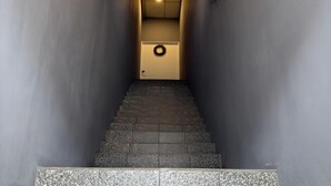 Un escalier étroit, dont les marches sont revêtues d’un matériau texturé, mène à une porte dotée d’une poignée circulaire.