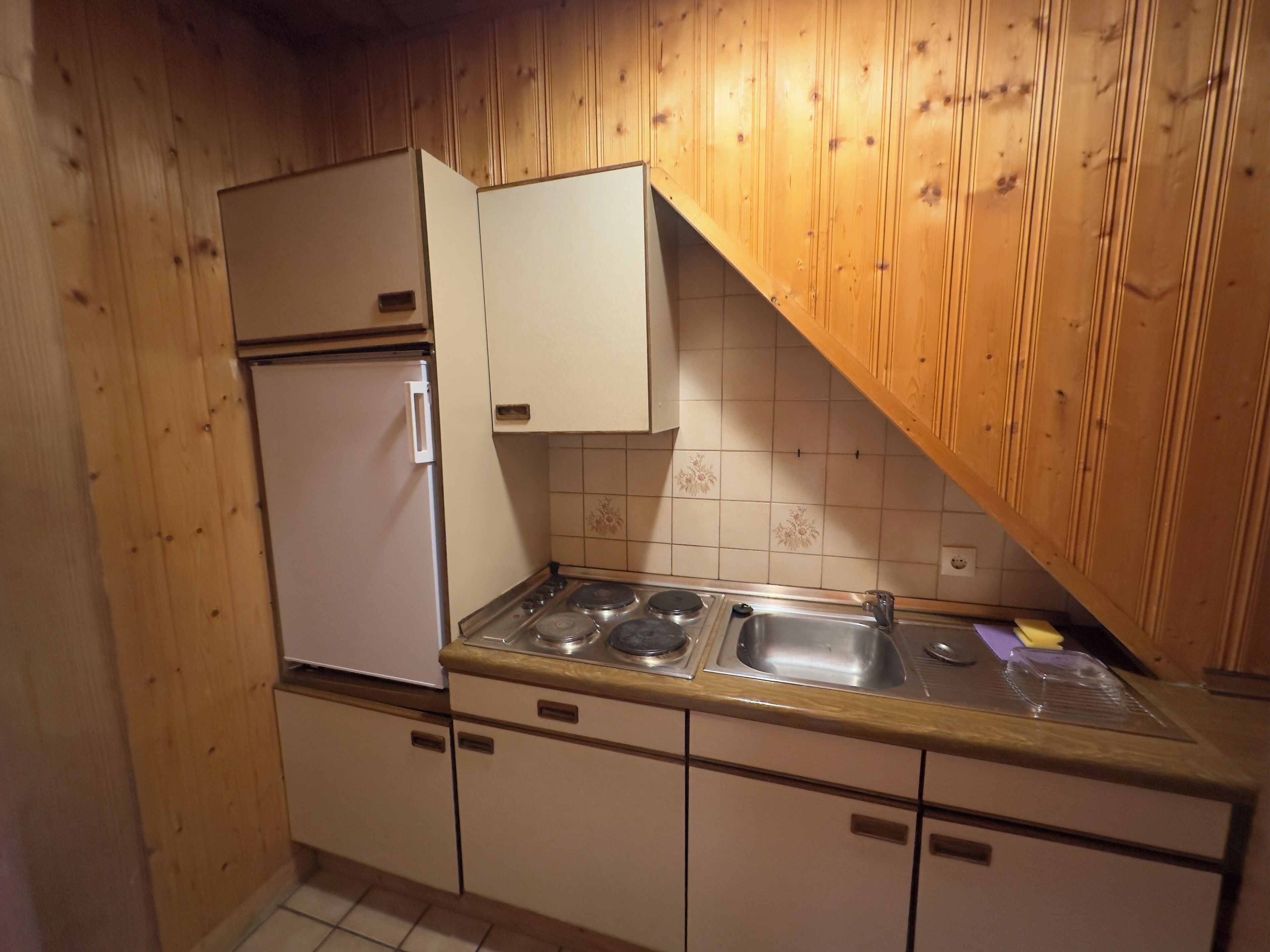A kitchen with wooden walls, a white refrigerator, a stove, and a sink.