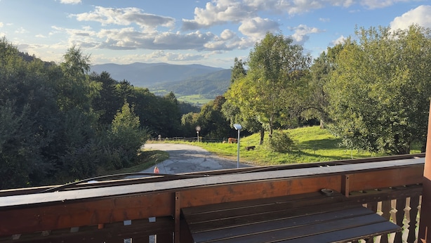 A wooden deck with a view of a rural landscape, including trees, a road, and distant mountains.